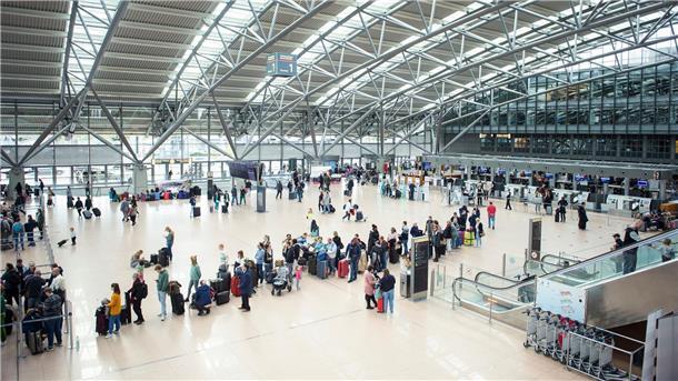 Warnstreiks in Berlin und Hamburg: Hunderte Flugausfälle Reisende stehen im Terminal des Flughafen Hamburg mit ihrem Gepäck in einer Warteschlange an einem Check in-Schalter.