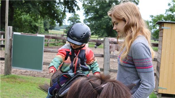 Kind auf Pony, daneben Frau mit langen Haaren