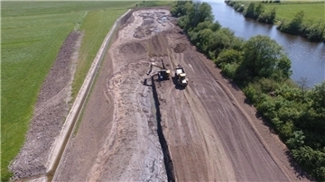 Luftaufnahm einer Baustelle: Links ist Weide, rechts ein Fluss zu sehen. 