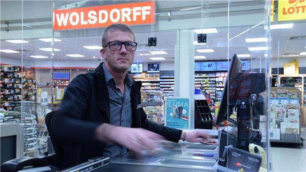 Ein Mann sitzt an der Kasse im Supermarkt und zieht die Artikel über den Scanner.