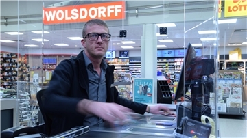 Ein Mann sitzt an der Kasse im Supermarkt und zieht die Artikel über den Scanner.