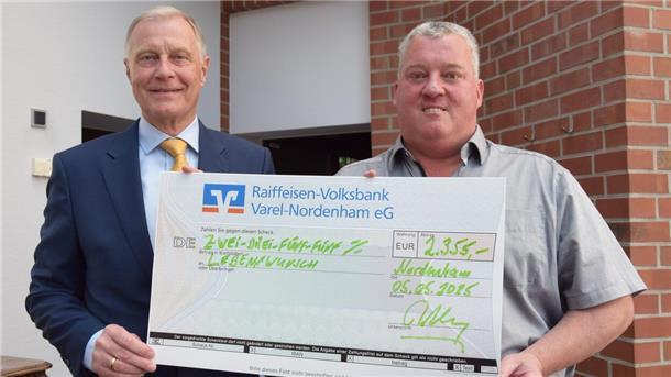 Zwei Männer stehen nebeneinander und halten einen großen Scheck in die Kamera. 