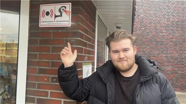 Mann zeigt auf Schild mit Kameraüberwachung