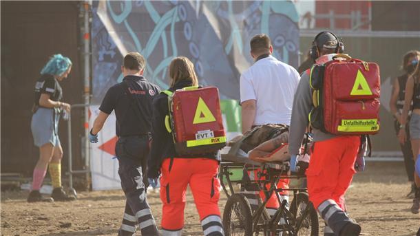 Ein Team von Sanitätern transportiert einen Patienten auf einer Trage über das Festivalgelände 