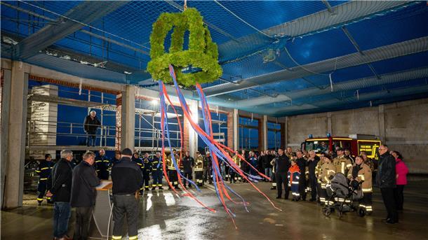 Ein Richtkranz hängt an der noch offenen Decke der Fahrzeughalle, die Gäste in Feuerwehrkleidung und Zivil lauschen den Grußworten. 