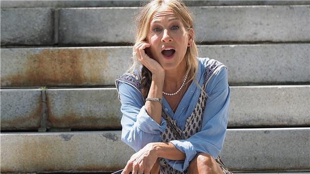 Sarah Jessica Parker sitzt auf der Treppe, ihr Kinn in die Hand gestützt.