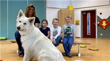 Ein Hund im Vordergrund, im Hintergrund drei Kinder und eine Erzieherin.
