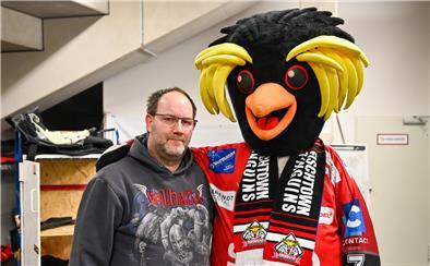 Ein Mann steht neben einem großen Pinguin-Maskottchen. 