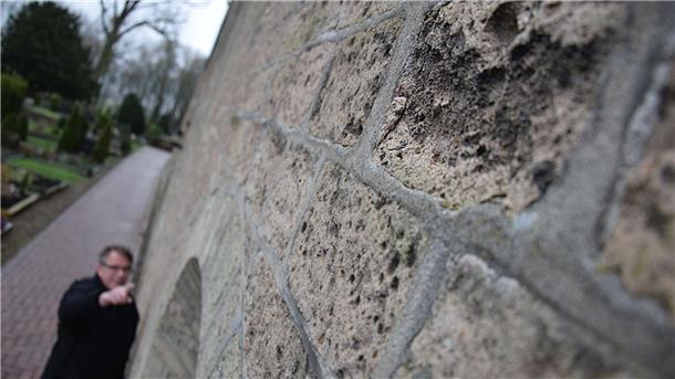 Mann zeigt auf Schäden an einer Mauer