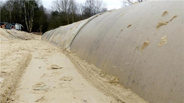 Schicht für Schicht wird der Sand in der Baugrube verdichtet, damit das Rohr fest sitzt. 
