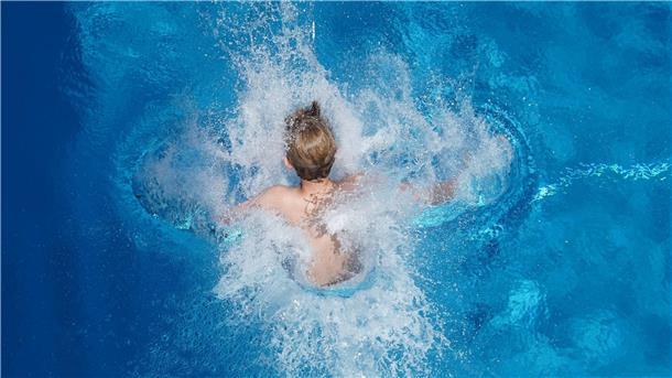 Ein Junge klatscht in einem Schwimmbad ins Wasser