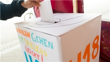 Eine Wahlurne, in der ein Stimmzettel eingeworfen wird.