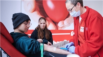 Ein junger Mann spendet Blut. Eine DRK-Mitarbeiterin setzt die Kanüle.