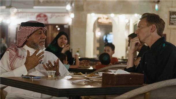 Khalid Salman sitzt mit dem ZDF-Journalisten Jochen Breyer in einer belebten Fußgängerzone in Doha.