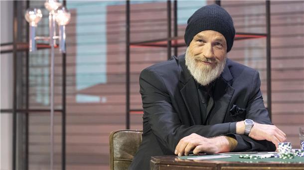 Torsten Sträter sitzt in einem Fernsehstudio vor einem Tisch.