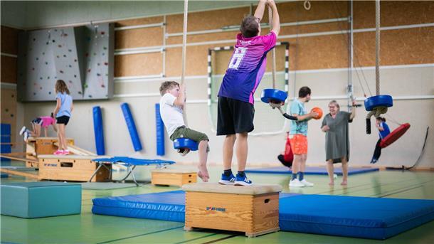 Kinder bewegen sich in einer Turnhalle in einer Bewegungslandschaft, schaukeln und balancieren.