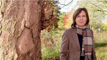 Eine Frau mit Schal steht neben einem Baum.