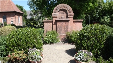 Ein Kriegerdenkmal im HintergrundDrumherum Sträucher und Blumenkübel.