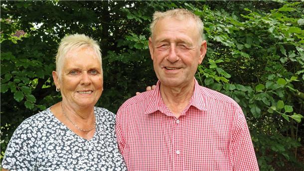 Ute und Henry Denker im Garten, rund 50 Jahre nach ihrer Hochzeit. Beide lächeln in die Kamera, im Hintergrund grünes Laub.