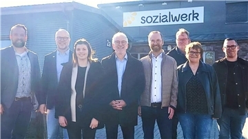 Acht Menschen stehen vor einer großen Halle mit der Aufschrift "sozialwerk". 