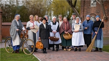 Männer und Frauen in historischen Kleidern stehen vor einer Mühle. 