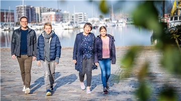 Sie sind die Familie des 1973 ausgewanderten Jugoslawen Franjo Spahic: Sein Sohn Marinko, sein Enkel Samuel, Ehefrau Susanne und Enkelin Olivia spazieren gern an der Kaje des Neuen Hafens entlang, an der nicht nur einst Spahics erster Arbeitsplatz war, sondern inzwischen auch das Auswandererhaus unter anderem seine Geschichte erzählt. Franjo Spahic ist 2016 verstorben. Sein Foto an der DAH-Fassade wird künftig an ihn erinnern. Foto: Hartmann