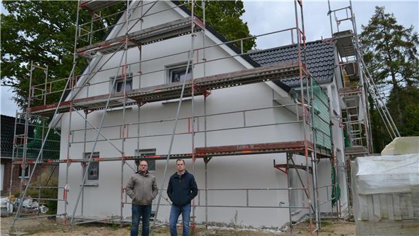 Hausbauer und Handwerksmeister vor einem unfertigen Haus.