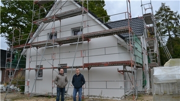 Hausbauer und Handwerksmeister vor einem unfertigen Haus.