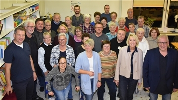 Große Gruppe von Frauen und Männern steht in einem Raum und guckt Richtung Kamera.