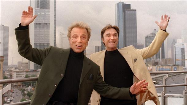 Siegfried & Roy reißen die Arme in die Höhe. Apple TV+ plant jetzt eine Serie über das Leben des Magier-Duos.