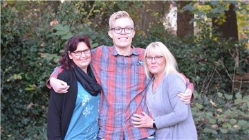 Zwei Frauen und ein junger Mann, Arm in Arm in einem Garten.