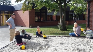 Kinder und Erwachsene an und in einem Sandkasten