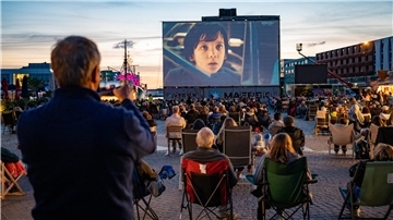 Im Fischereihafen ist eine riesige Leinwand aufgebaut, auf der ein Film zu sehen ist. Davor sitzen Hunderte Besucher. 