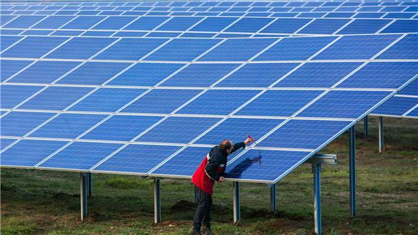 Ein Mann schraubt an einem Solarmodul auf einer Wiese.