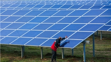 Ein Mann schraubt an einem Solarmodul auf einer Wiese.