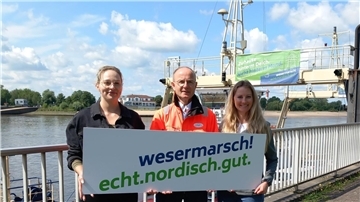 Sophia Wolfram (Gemeinde Ovelgönne, Mitglied der Steuerungsgruppe Standortmarketing), Andreas Bettray (Geschäftsführer der Fähren Bremen-Stedingen) und Isa Grube (Wirtschaftsförderung Wesermarsch) präsentieren den Slogan der Kampagne.