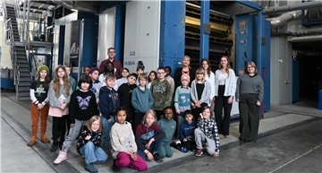 Viele Schülerinnen und Schüler stehen mit Lehrern vor einer großen Druckmaschine.
