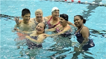 sechs gut gelaunte Personen in Badebekleidung in einem Schwimmbecken