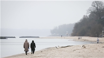 Spaziergänger mit Hunden sind bei leichtem Nieselregen am Strand von Schilksee bei Kiel.