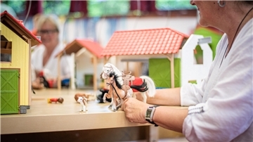 Pferdepuppen und Miniaturställe. Eine Frau hält die Spielzeuge in ihren Händen.