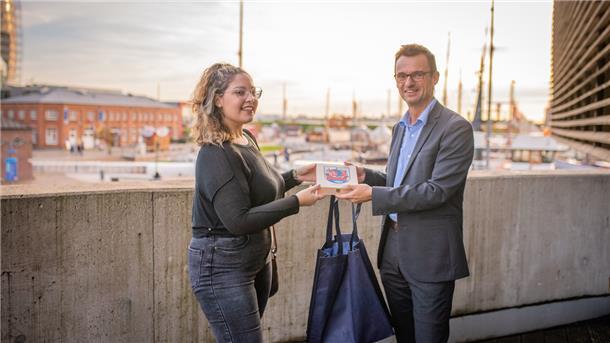 Stadtrat Michael Frost begrüßt die Spanierin Cecilia Hernandéz Garcia in Bremerhaven. Die Begrüßungstasche für die Kita-Fachkraft enthält unter anderem eine Fahrt mit dem Hafenbus. Foto: Hartmann