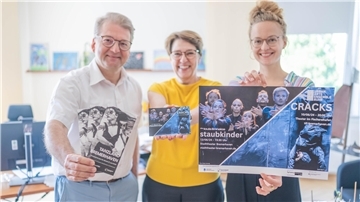 Ein Mann und zwei Frauen stehen lächelnd nebeneinander und halten Flyer und Plakate zum "Tanzland Bremerhaven" in die Kamera