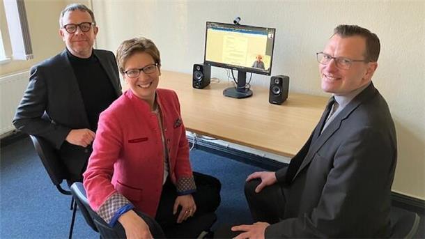 Zwei Herren (links und rechts) lächeln, eine Frau (Mitte) auch. Auf einem Schreibtisch ist ein Bildschirm zu sehen, der eingeschaltet ist. Der Start der Online-Rechtsantragstelle im Arbeitsgericht Bremen-Bremerhaven erleichtert den Bürgern den Zugang zur Justiz, indem sie Anträge und Klagen bequem von zuhause aus einreichen können.