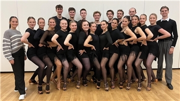 Eine Tanzformation aus jungen Frauen und Männern, schwarz gekleidet, posiert mit ihren Trainern für die Kamera.