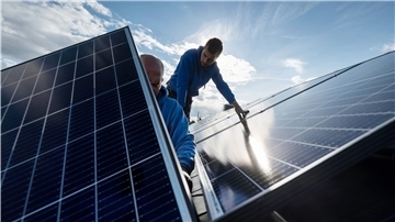Männer montieren Photovoltaikmodule auf dem Dach eines Gebäudes. 