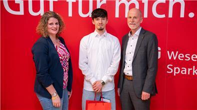 Stefanie Klüver, Leiterin Geschäftsstelle Kreissportbund Cuxhaven und Rolf Sünderbruch, Vorstandsvorsitzender der Weser-Elbe Sparkasse überreichen Karateka Aaric Liam Lück (Mitte) das Sportstipendium für 2025.