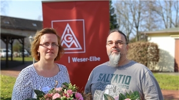 Frau mit Brille und Blumen, rote Fahne, Mann mit Brille und grauem Bart