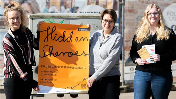 Zwei Frauen halten ein Plakat in den Händen, die dritte Frau hält Flyer in ihren Händen.