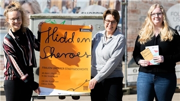 Zwei Frauen halten ein Plakat in den Händen, die dritte Frau hält Flyer in ihren Händen.