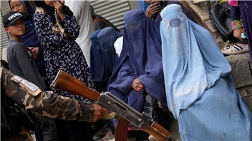 Straßenszene in Kabul: Ein bewaffneter Taliban-Kämpfer steht neben vollverschleierten Frauen. Die Islamisten haben Frauenrechte massiv eingeschränkt.